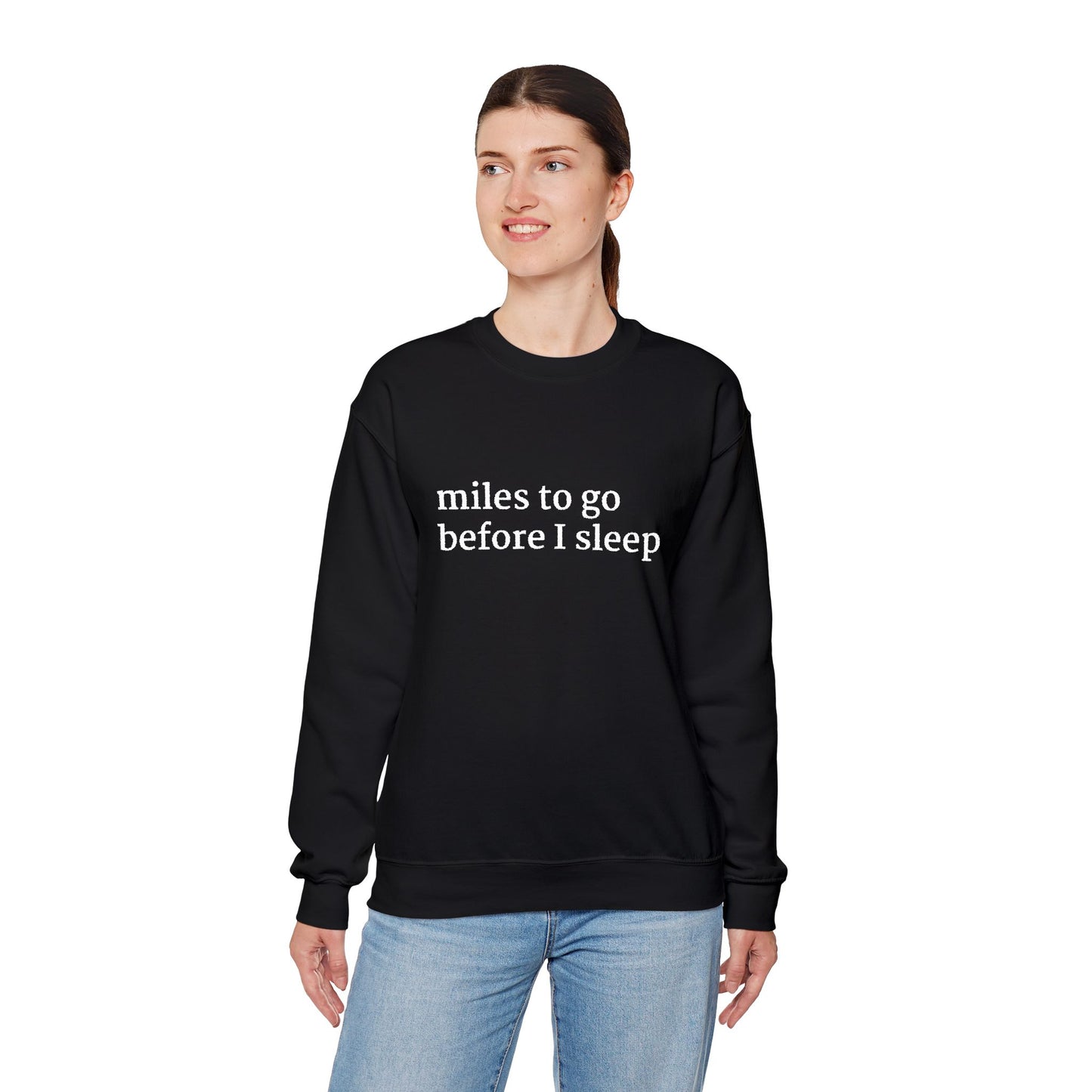 Model standing wearing a black crewneck sweatshirt with white text reading ‘miles to go before I sleep,’ paired with light blue jeans.