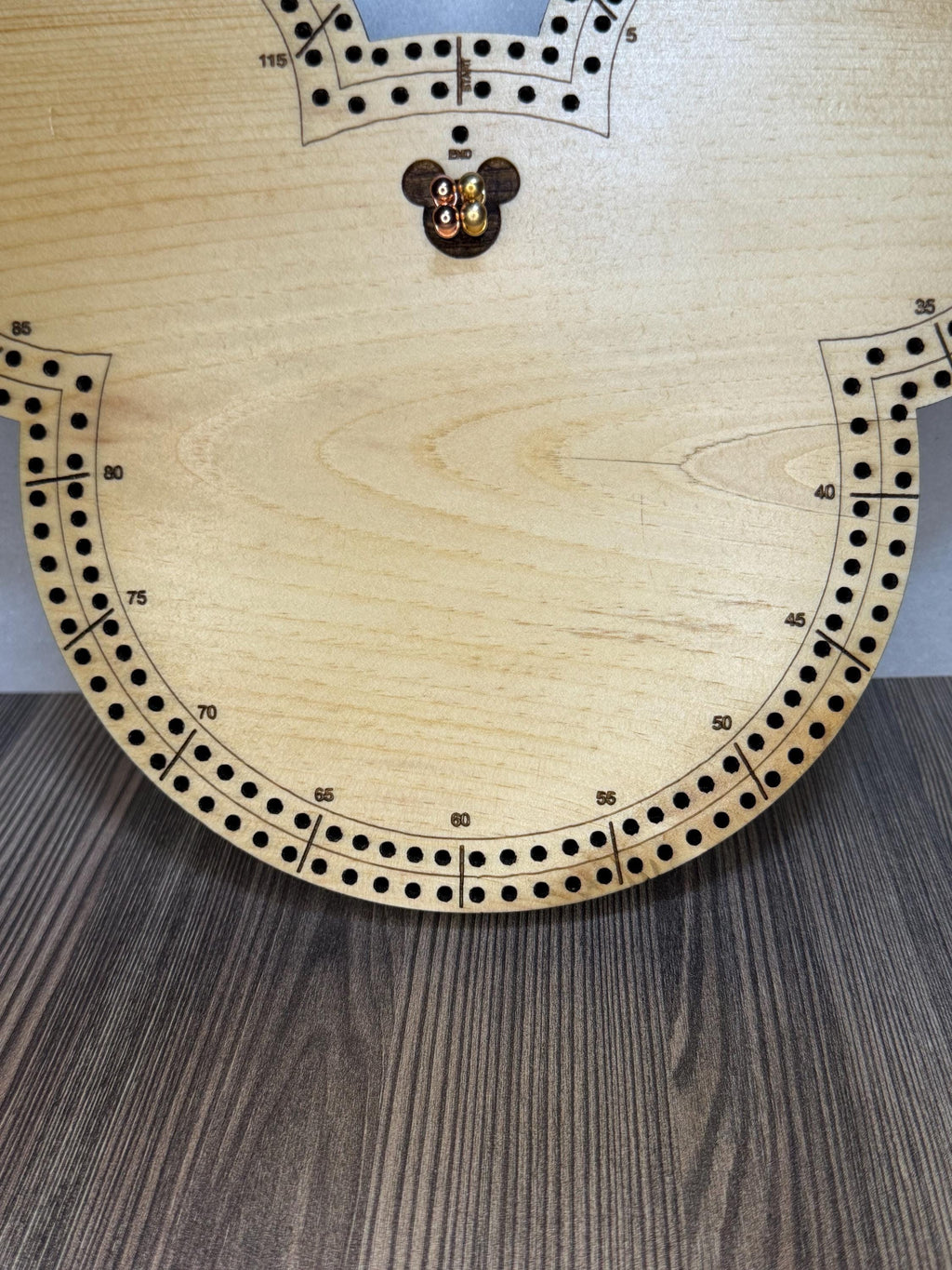 Close-up of the lower section of a handmade wooden cribbage board showing engraved scoring numbers, evenly spaced peg holes, and natural wood grain detail.