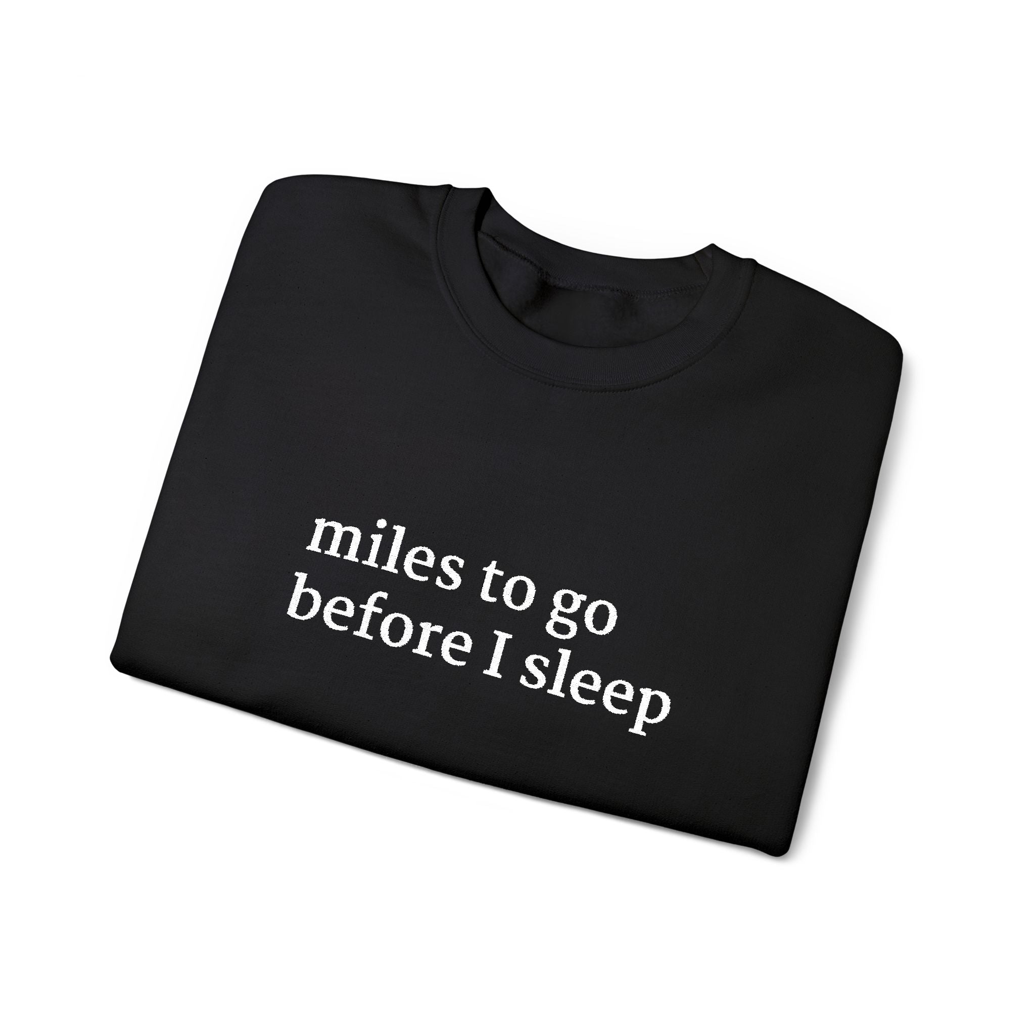 Folded black crewneck sweatshirt with white text reading ‘miles to go before I sleep’ on the front.