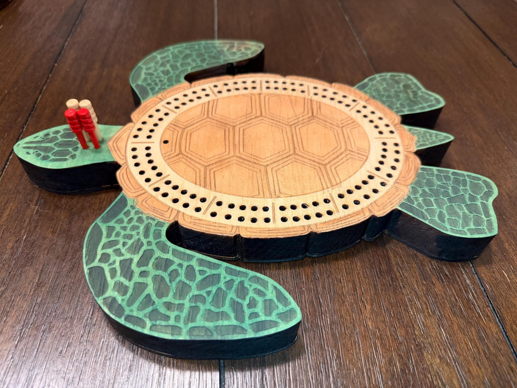 Overhead view of a wooden turtle cribbage board with four cribbage pegs placed at the starting area, showing the full board layout and engraved details.