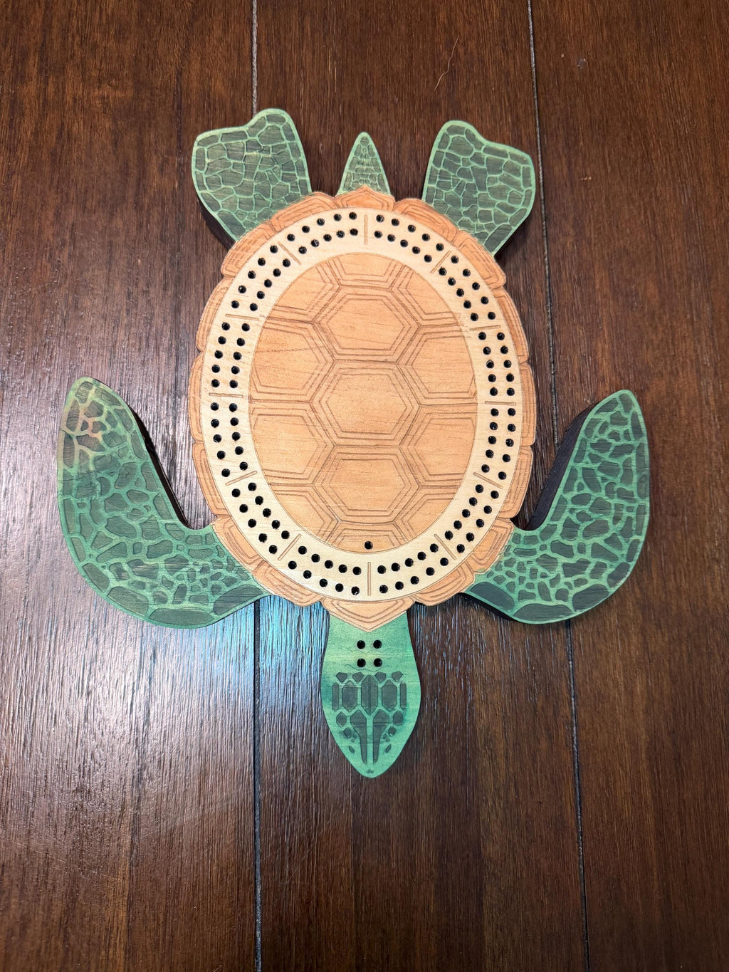 Centered overhead image of a handcrafted wooden turtle cribbage board displaying the complete 60-hole peg track and engraved shell design.