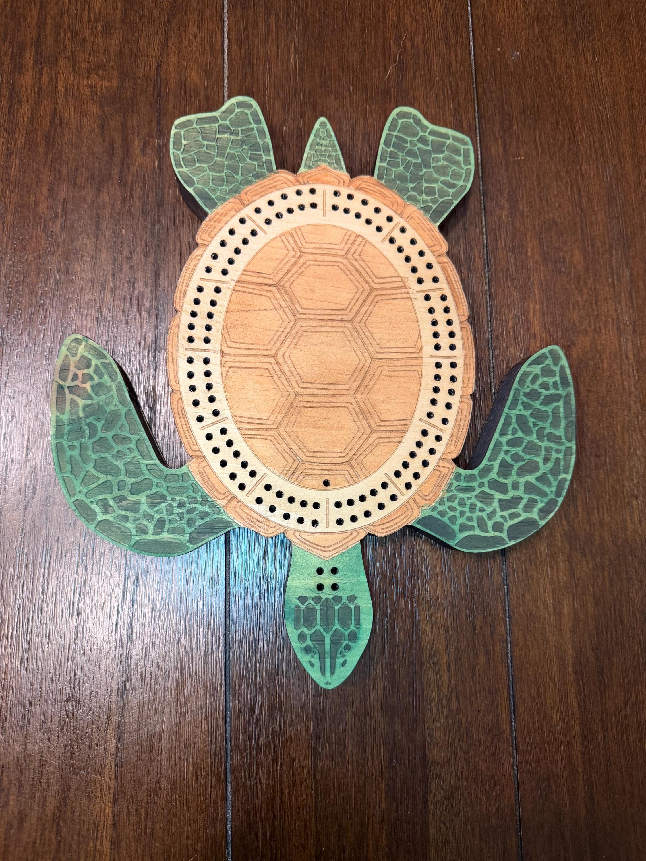 Centered overhead image of a handcrafted wooden turtle cribbage board displaying the complete 60-hole peg track and engraved shell design.